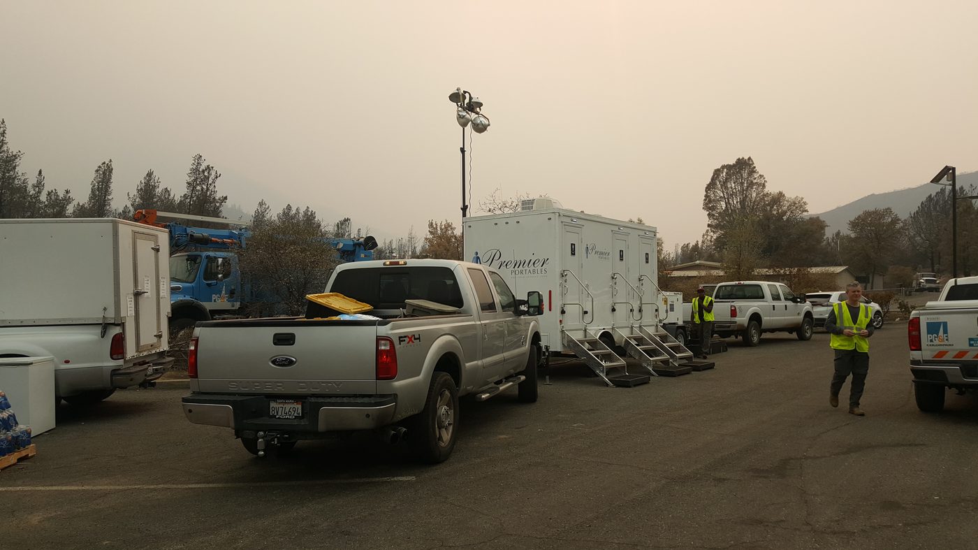 Restroom trailer at a public utility staging area with PG&E trucks and field crews