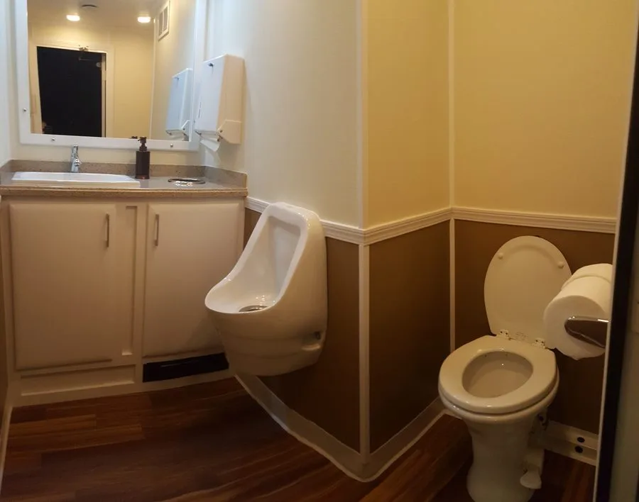 Men's restroom station inside a 3-station trailer with urinal, toilet, vanity sink and granite countertop