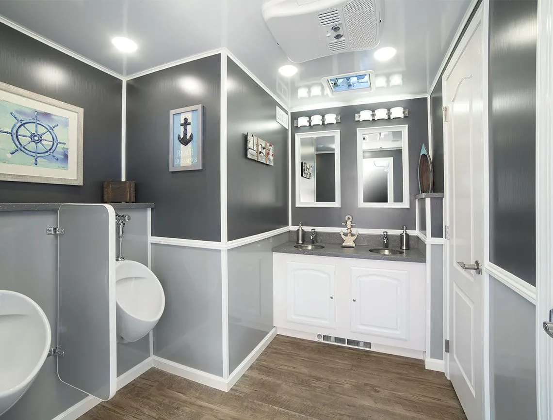 Interior of an 8-station restroom trailer showing urinals with privacy dividers, a double-sink vanity, mirrors, and finished walls