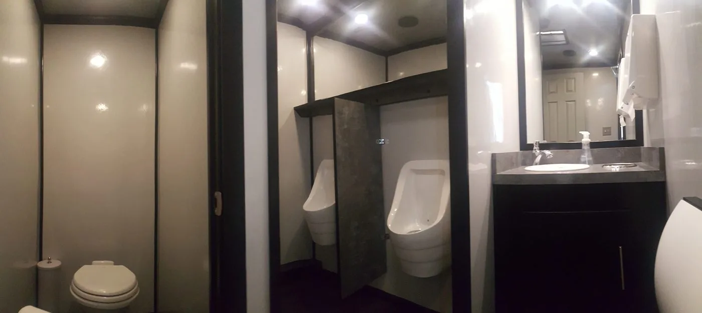 Panoramic interior of a restroom trailer showing private stall, urinals with privacy dividers, dark trim cabinetry and granite vanity