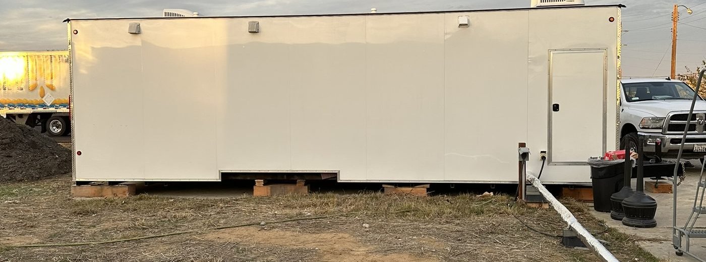 Rear of restroom trailer showing septic hookup pipe running to underground septic tank at Walmart truck school site