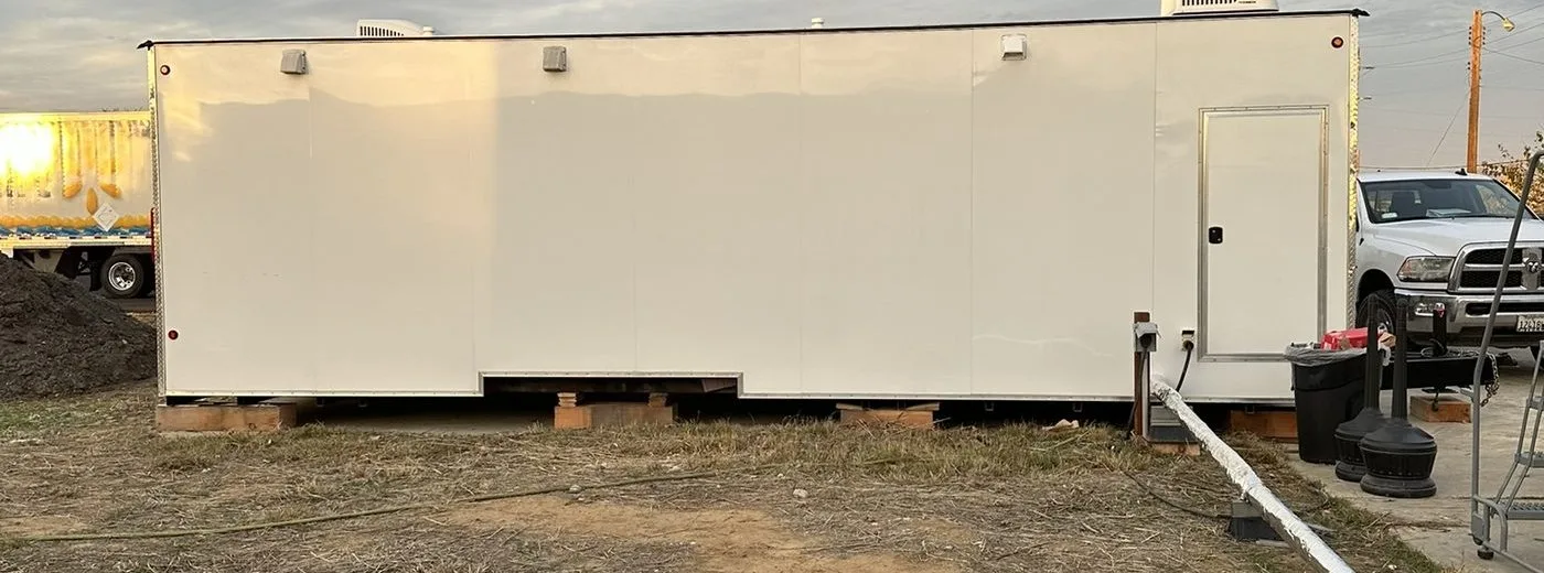 Rear of restroom trailer showing septic hookup pipe running to underground septic tank at Walmart truck school site
