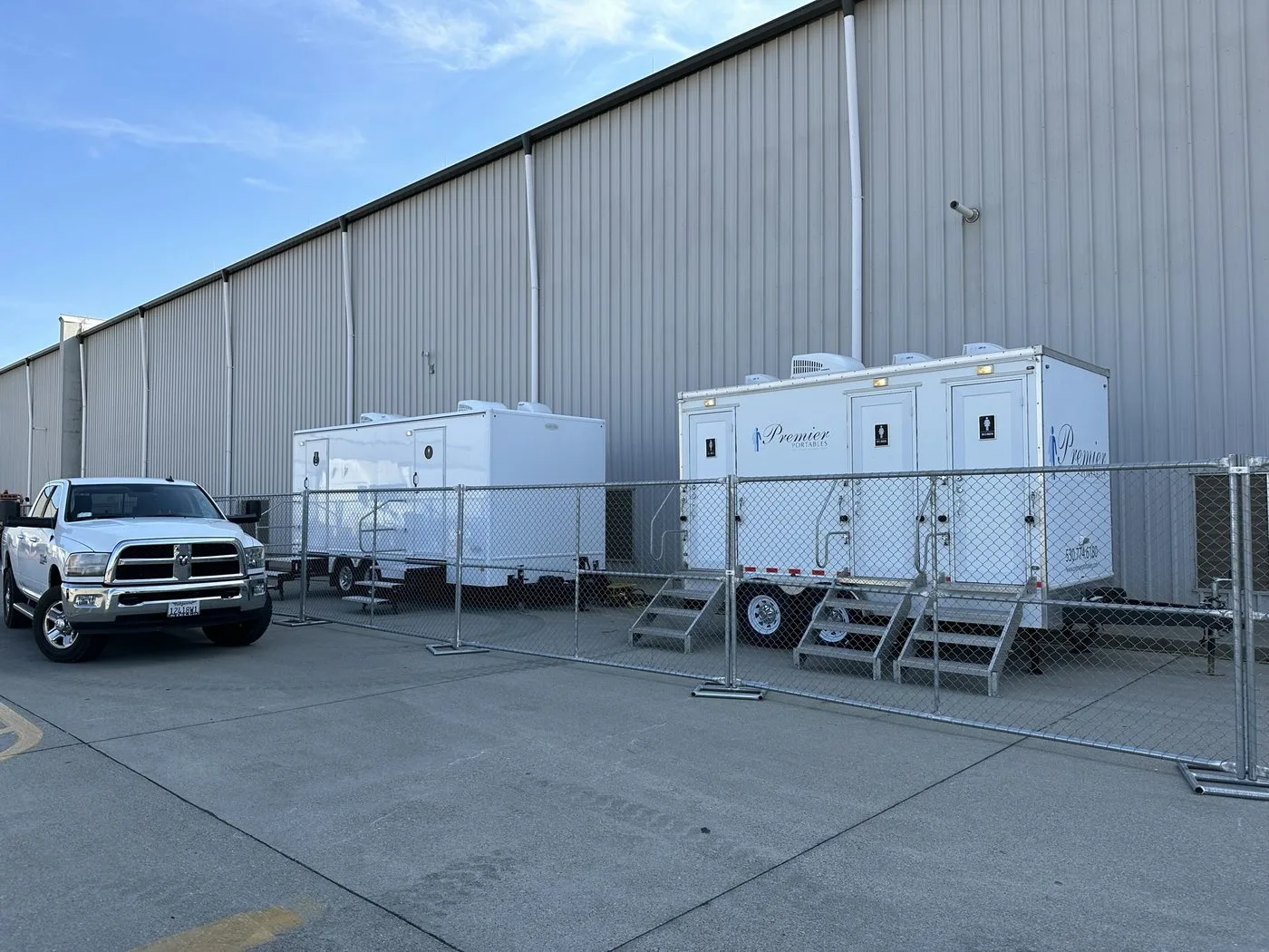 Two Premier Portables restroom trailers behind chain-link security fencing at a distribution center