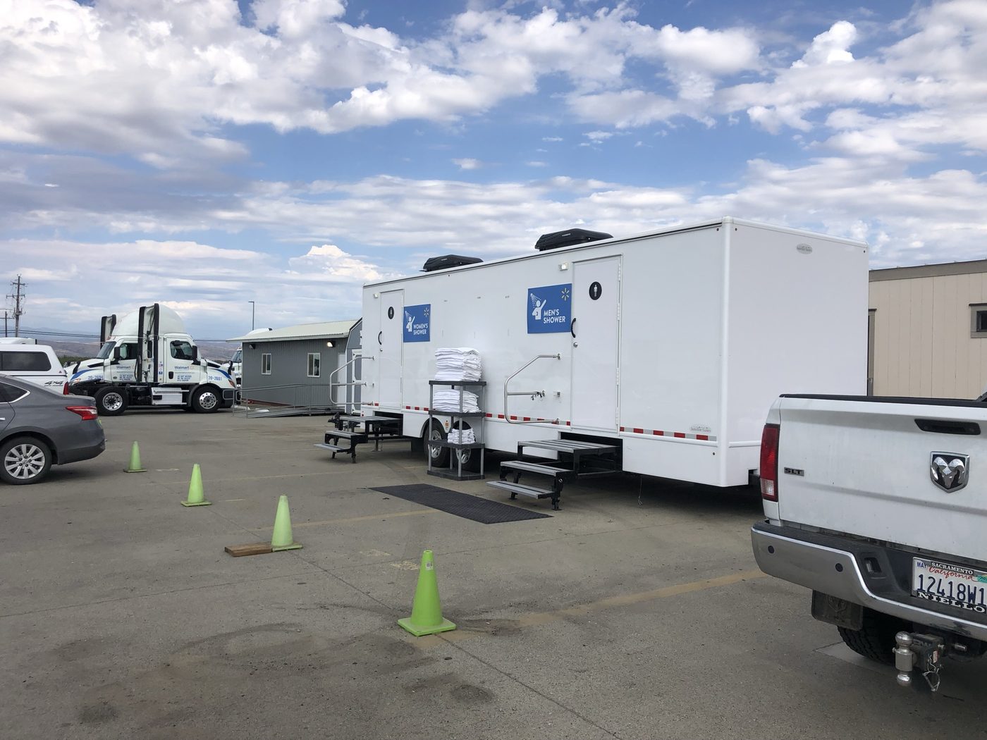 Walmart shower trailer with Men's and Women's Shower signage at the distribution center, Walmart fleet trucks visible in background