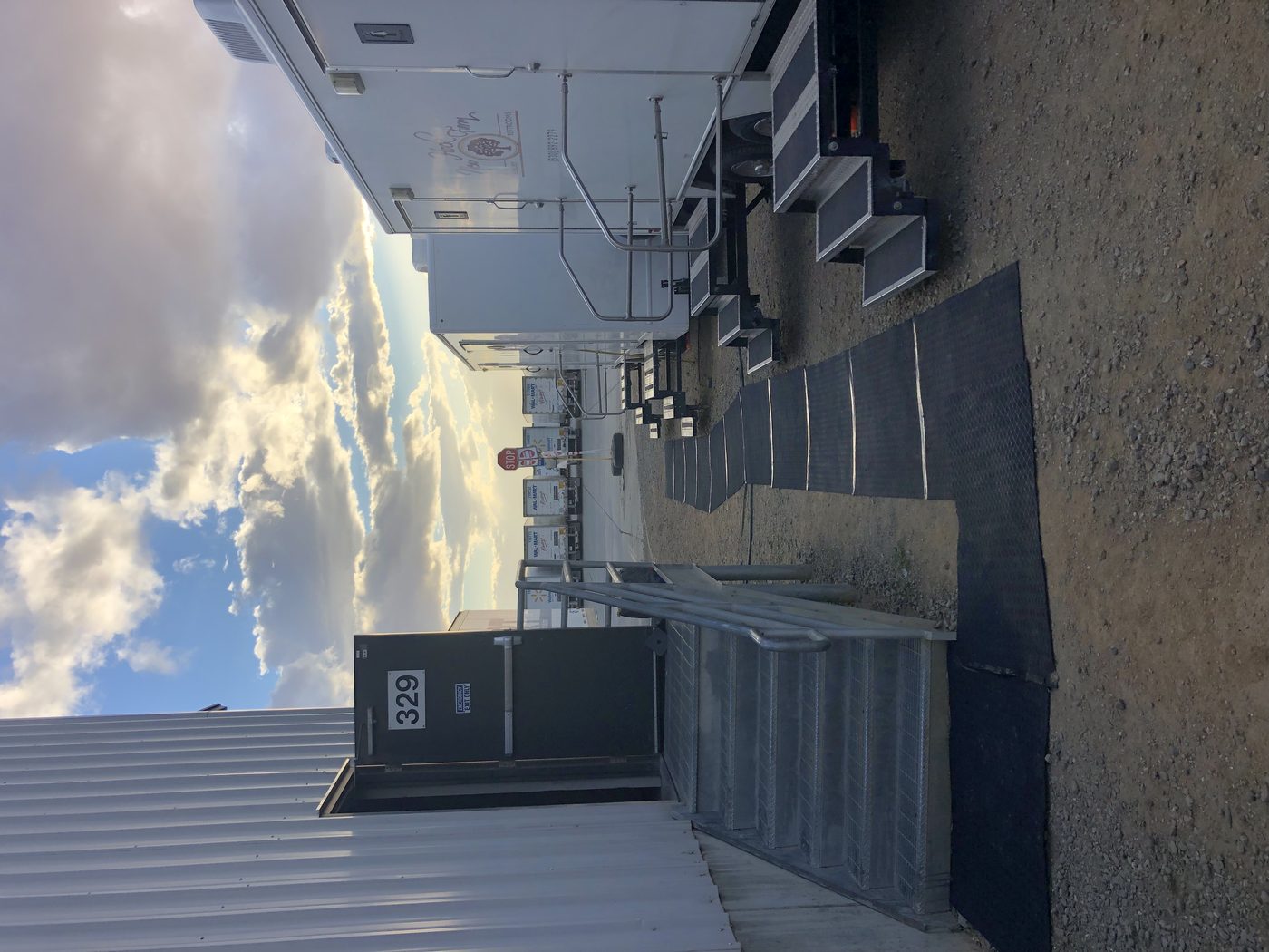 Rubber walkway mats connecting the distribution center exit door to a row of restroom trailers, Walmart fleet trucks visible in background